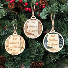 Arizona-shaped 'First Christmas in Arizona' ornament hanging on a festive holiday tree with glowing lights and lush green branches. A perfect keepsake to celebrate a special first Christmas in the Grand Canyon State.