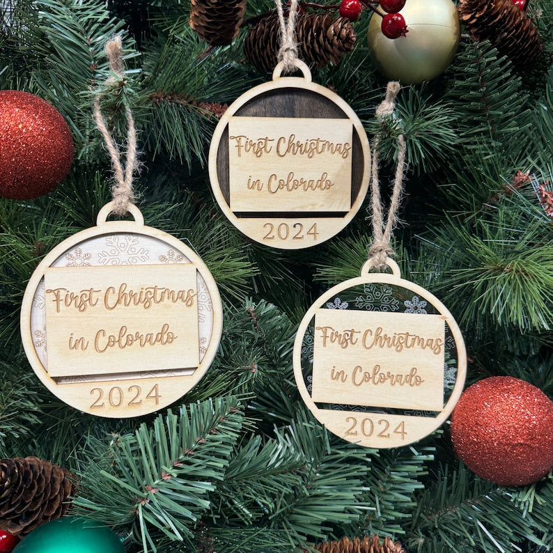 Colorado-shaped 'First Christmas in Colorado' ornament adorning a sparkling holiday tree with twinkling lights and evergreen branches. A perfect keepsake to celebrate a memorable first Christmas in the Centennial State, evoking the beauty and spirit of Colorado's winter wonderland.