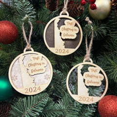 Delaware-shaped 'First Christmas in Delaware' ornament hanging on a festive holiday tree adorned with twinkling lights and evergreen branches. A charming keepsake to celebrate a special first Christmas in the First State, full of warmth and holiday cheer.