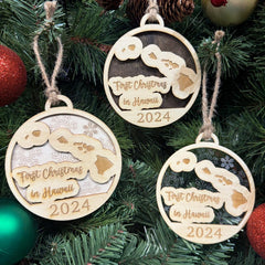 Hawaii-shaped First Christmas in Hawaii ornament hanging on a vibrant holiday tree with twinkling lights and tropical greenery. A unique keepsake to celebrate a memorable first Christmas in the Aloha State, capturing the island spirit and festive cheer.