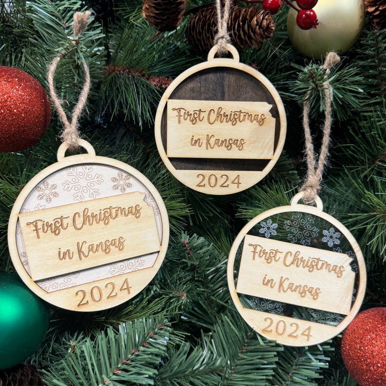 Kansas-shaped First Christmas in Kansas ornament hanging on a twinkling holiday tree with glowing lights and vibrant greenery. A perfect keepsake to celebrate a memorable first Christmas in the Sunflower State, capturing its wide-open skies and warm holiday spirit.