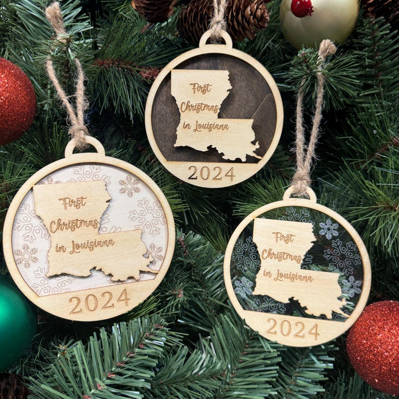 Louisiana-shaped First Christmas in Louisiana ornament hanging on a festive holiday tree with twinkling lights and lush greenery. A perfect keepsake to celebrate a lively first Christmas in the Pelican State, capturing its unique culture and vibrant holiday spirit.