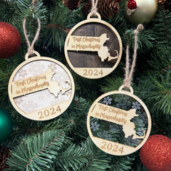 Massachusetts-shaped First Christmas in Massachusetts ornament hanging on a festive holiday tree with twinkling lights and evergreen branches. A perfect keepsake to celebrate a memorable first Christmas in the Bay State, reflecting its rich history and New England charm.