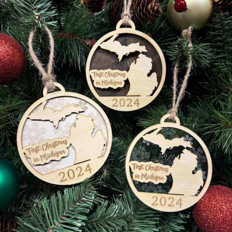 Michigan-shaped First Christmas in Michigan ornament hanging on a sparkling holiday tree with twinkling lights and lush greenery. A perfect keepsake to celebrate a memorable first Christmas in the Great Lakes State, capturing its winter beauty and festive spirit.