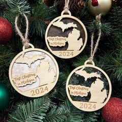 Michigan-shaped First Christmas in Michigan ornament hanging on a sparkling holiday tree with twinkling lights and lush greenery. A perfect keepsake to celebrate a memorable first Christmas in the Great Lakes State, capturing its winter beauty and festive spirit.