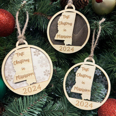 Mississippi-shaped First Christmas in Mississippi ornament hanging on a twinkling holiday tree with glowing lights and lush greenery. A perfect keepsake to celebrate a memorable first Christmas in the Magnolia State, capturing its southern charm and festive spirit.