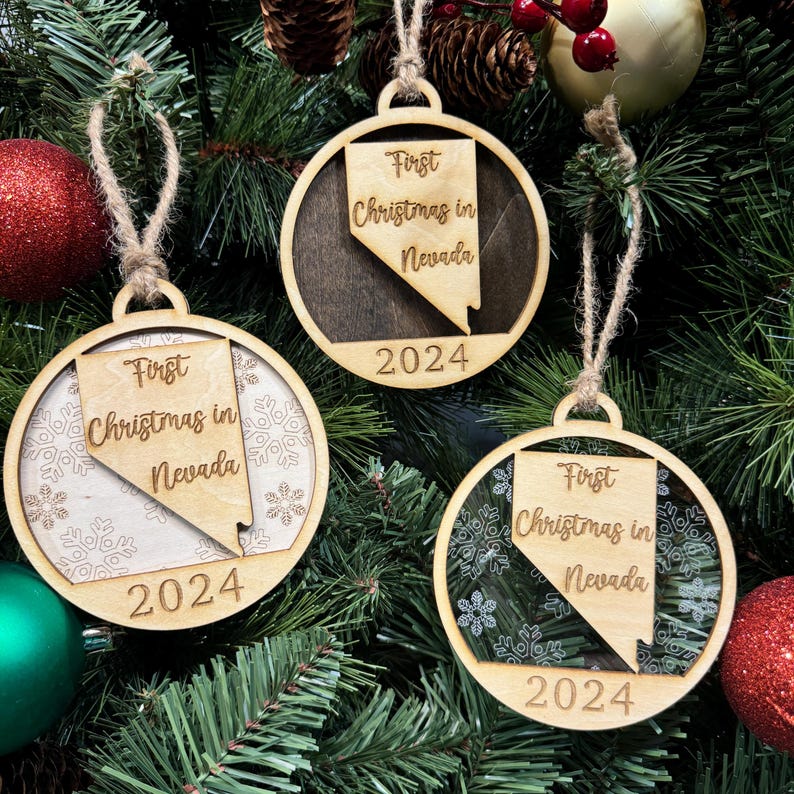 Nevada-shaped First Christmas in Nevada ornament hanging on a glowing holiday tree with twinkling lights and festive greenery. A perfect keepsake to celebrate a sparkling first Christmas in the Silver State, capturing its unique desert beauty and holiday spirit.