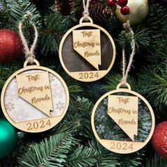 Nevada-shaped First Christmas in Nevada ornament hanging on a glowing holiday tree with twinkling lights and festive greenery. A perfect keepsake to celebrate a sparkling first Christmas in the Silver State, capturing its unique desert beauty and holiday spirit.