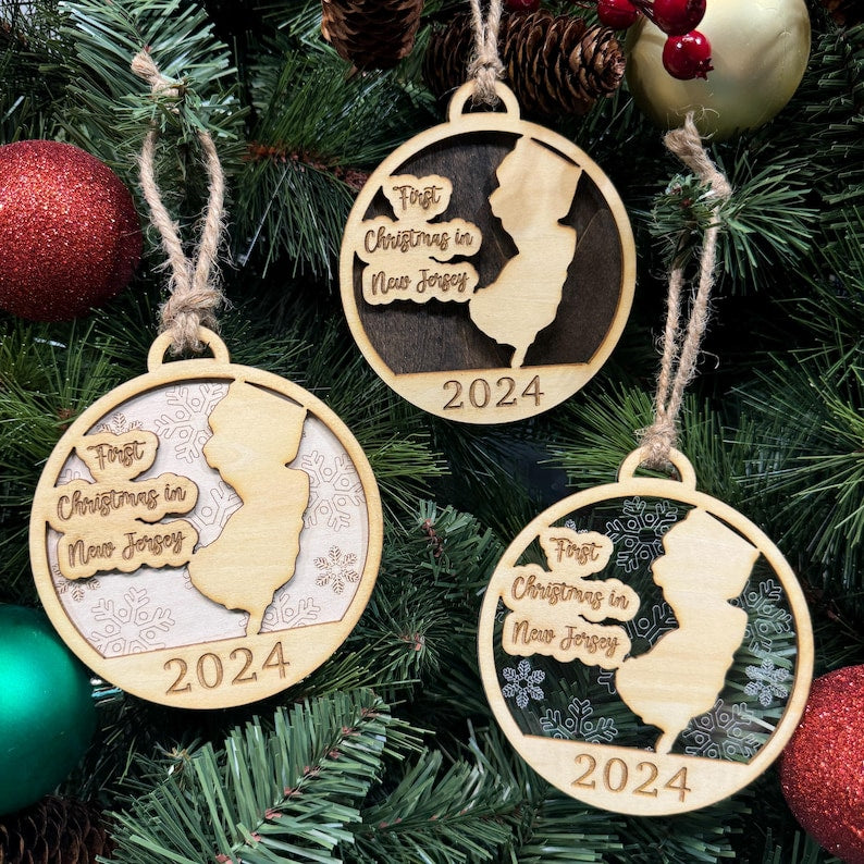 New Jersey-shaped First Christmas in New Jersey ornament hanging on a sparkling holiday tree with twinkling lights and lush greenery. A perfect keepsake to celebrate a special first Christmas in the Garden State, capturing its vibrant spirit and festive charm.
