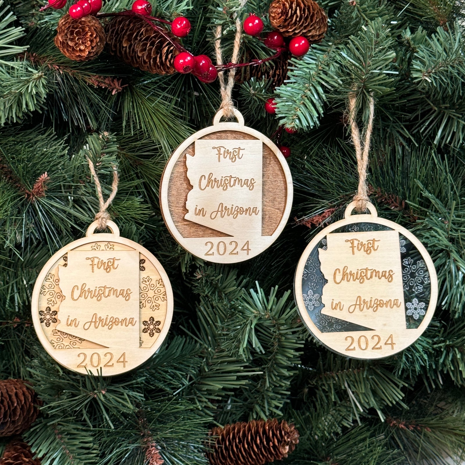 Arizona-shaped 'First Christmas in Arizona' ornament hanging on a festive holiday tree with glowing lights and lush green branches. A perfect keepsake to celebrate a special first Christmas in the Grand Canyon State.
