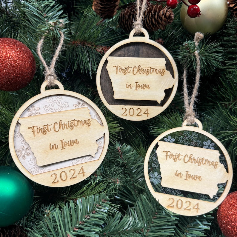 Iowa-shaped First Christmas in Iowa ornament hanging on a festive holiday tree with glowing lights and lush greenery. A charming keepsake to celebrate a cozy first Christmas in the Hawkeye State, reflecting its heartland spirit and seasonal cheer.