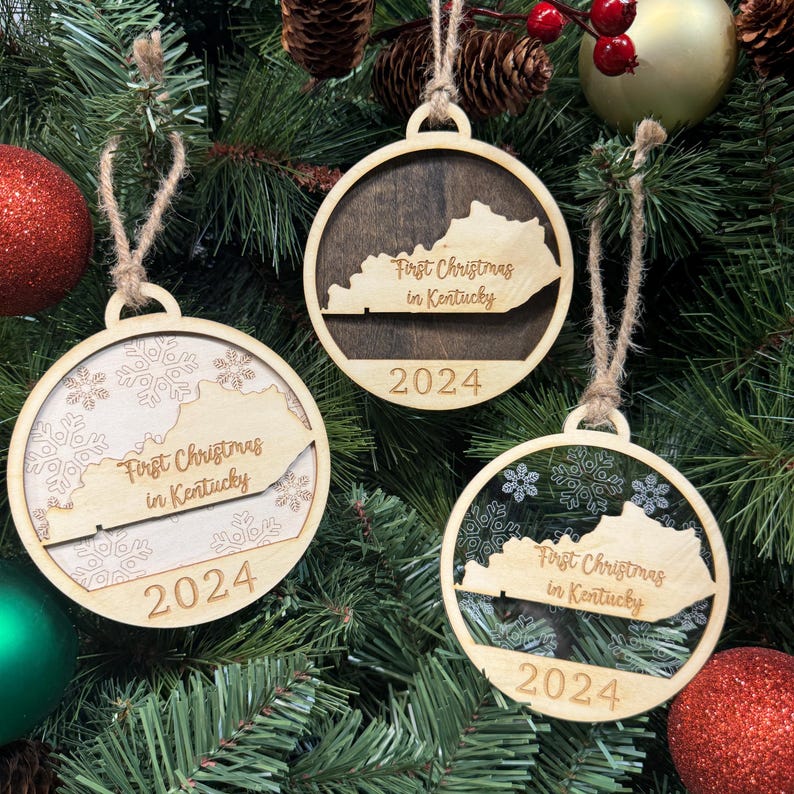 Kentucky-shaped First Christmas in Kentucky ornament hanging on a festive holiday tree with twinkling lights and evergreen branches. A charming keepsake to celebrate a memorable first Christmas in the Bluegrass State, filled with southern hospitality and holiday cheer.