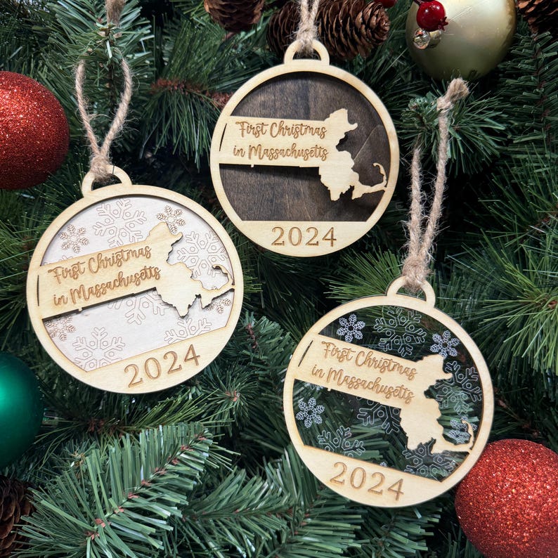 Massachusetts-shaped First Christmas in Massachusetts ornament hanging on a festive holiday tree with twinkling lights and evergreen branches. A perfect keepsake to celebrate a memorable first Christmas in the Bay State, reflecting its rich history and New England charm.